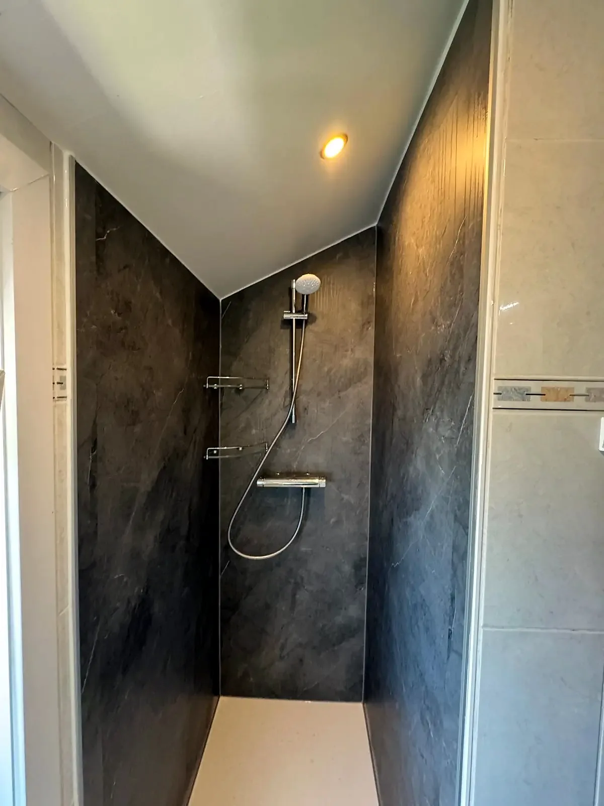 Douche onder schuin plafond met donkere marmerlook wandpanelen