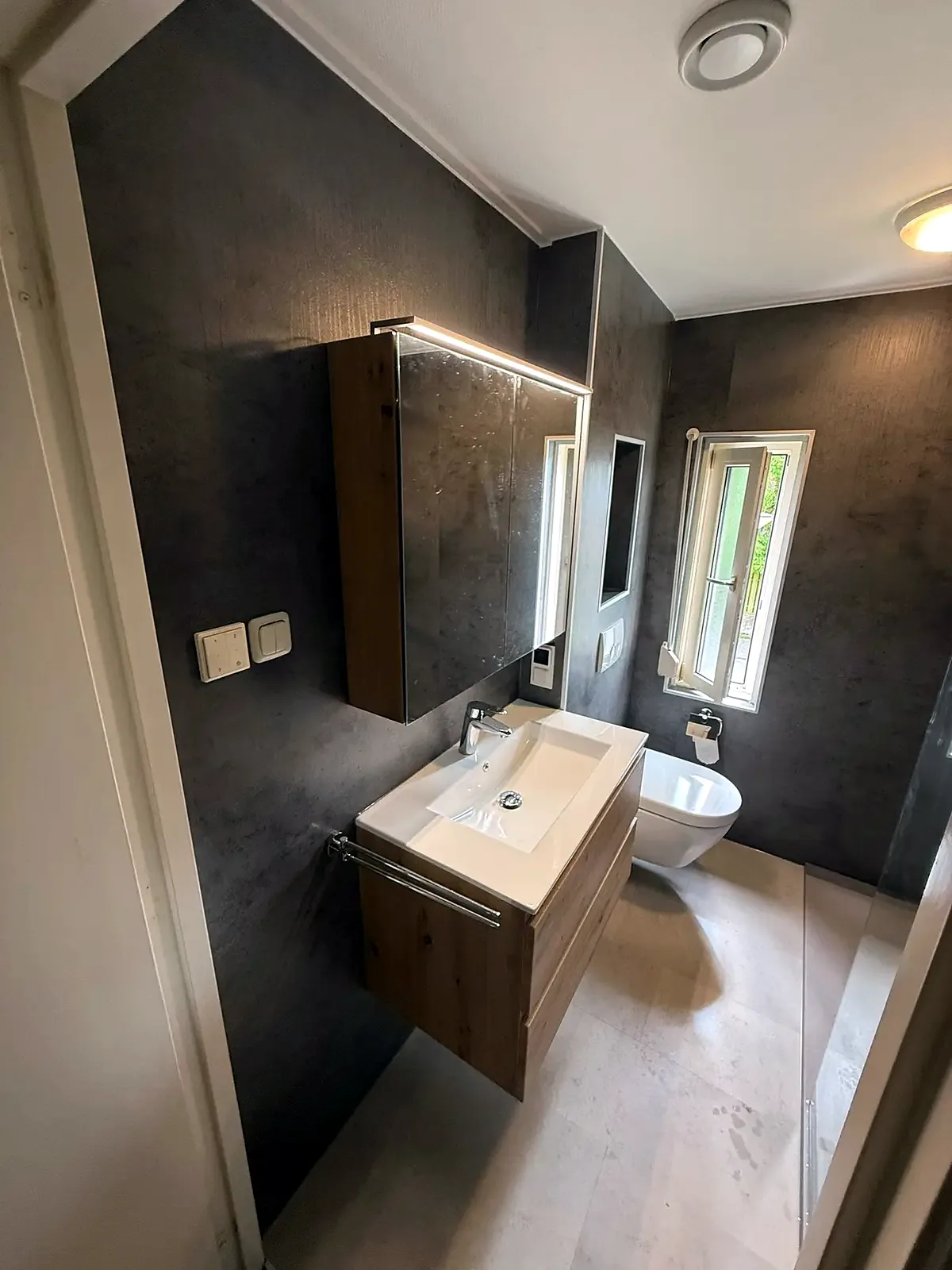 Badkamer met donkere wandpanelen, eiken wastafelmeubel en spiegelkast met verlichting