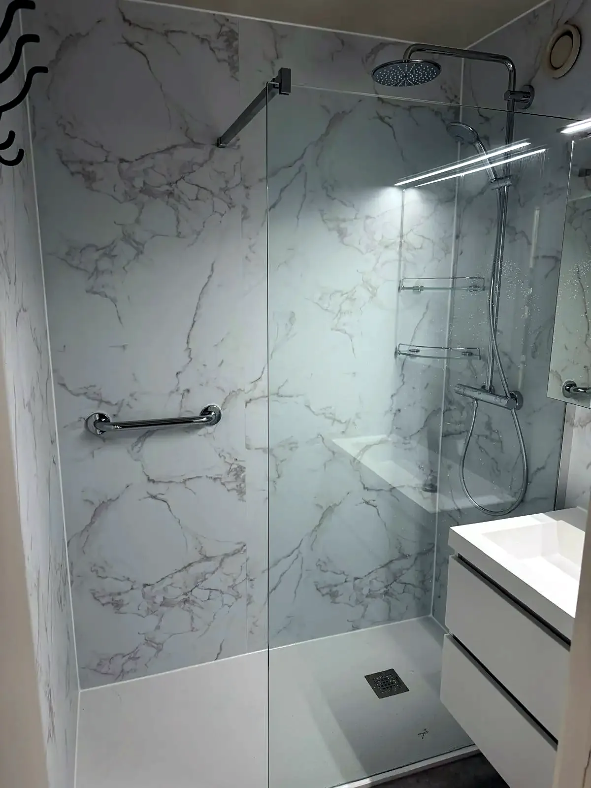Ruime inloopdouche met witte marmerlook wandpanelen, regendouche en glazen wand